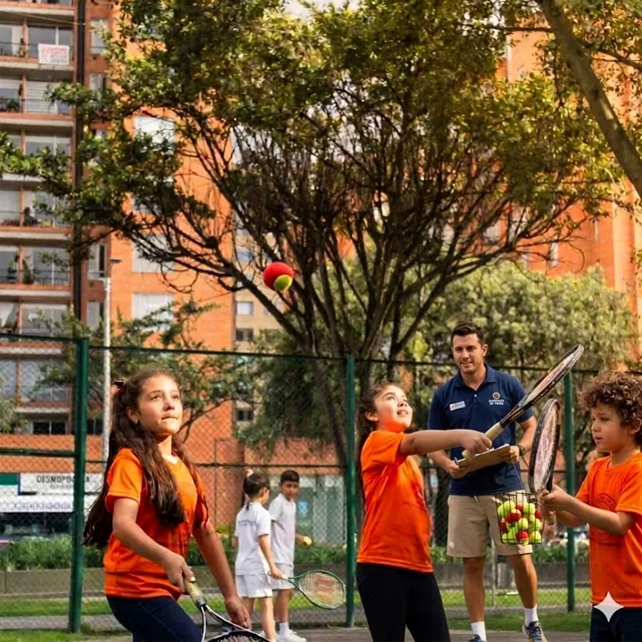 Instructor de tenis con camiseta naranja explica un ejercicio a sus alumnos.